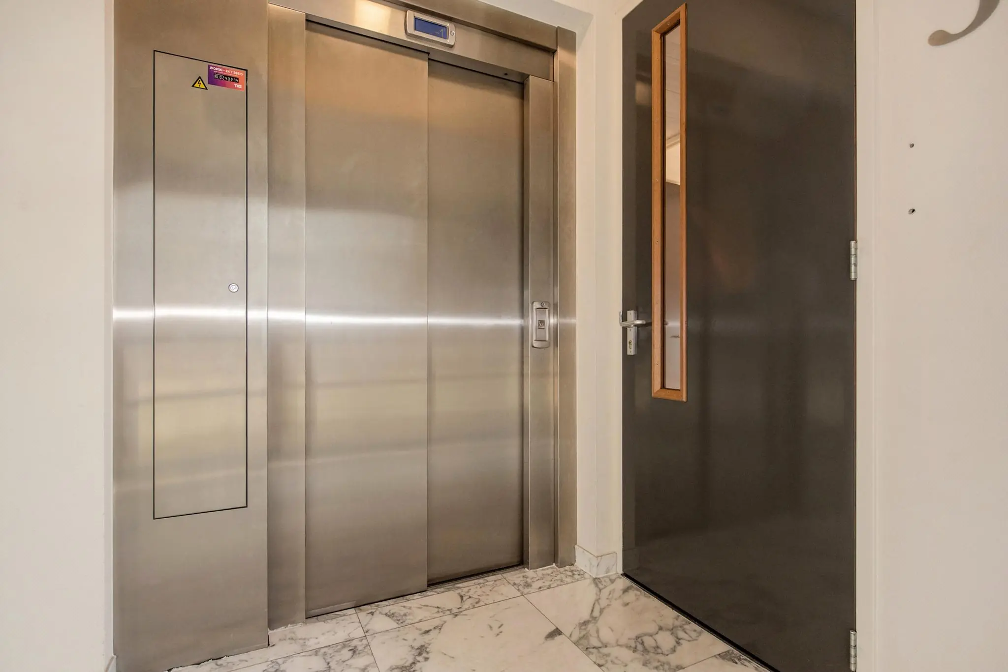 RVS-liftdeur in de hal van een gebouw aan de Laan van Vredenoord, met marmeren vloer en een openstaande binnendeur.